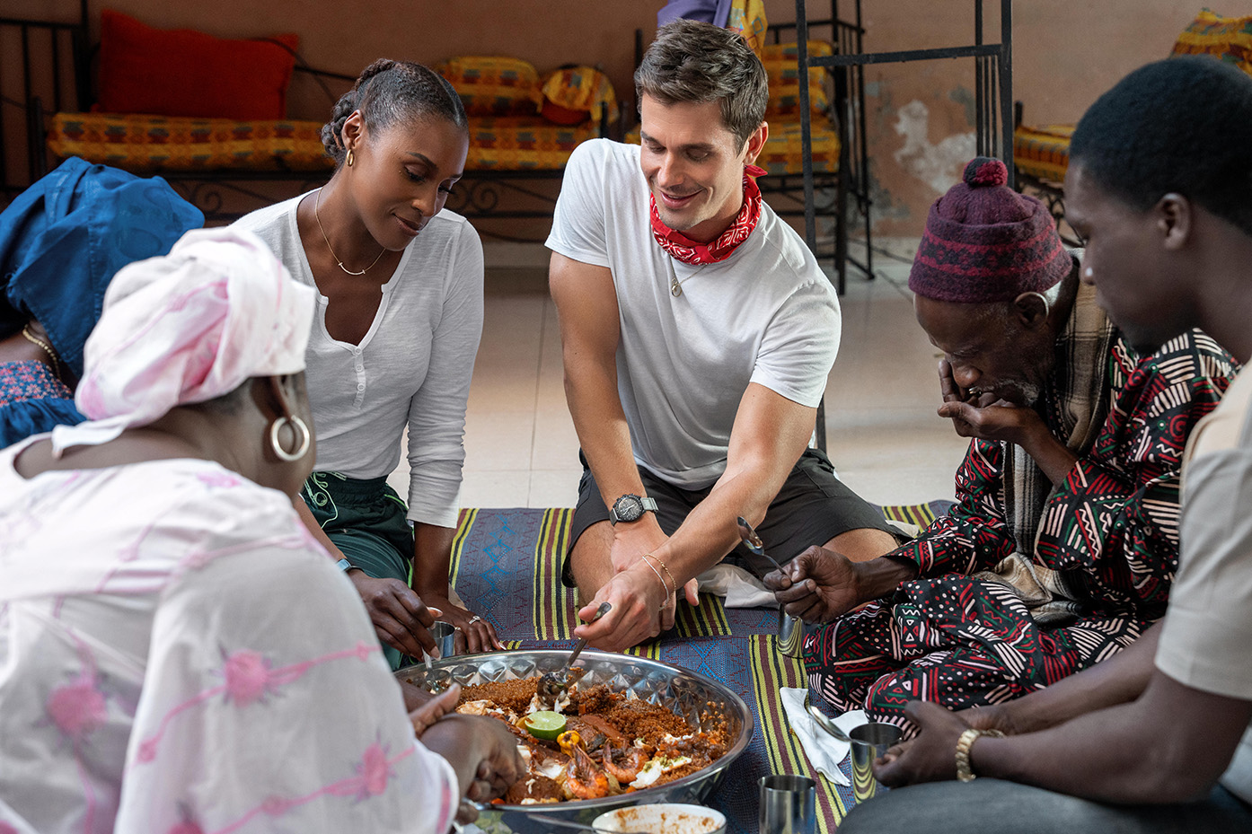 Mama Yacine, Fatima Fall, Issa Rae, Antoni Porowski, Papa Abdoulaye Sene and Hamade Ndiaye sit in a circle eating Ceebu jën.